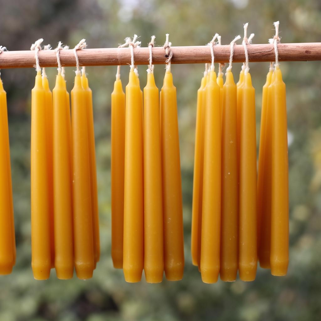 Pairs of golden hand-dipped beeswax tapers hung from a wooden rod to cure