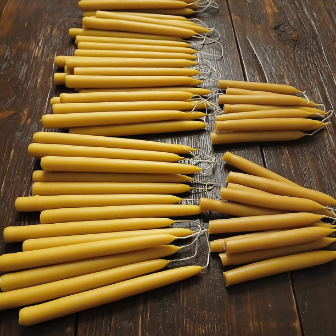 Finished bundles of hand-dipped beeswax tapers laid on a wooden worktable