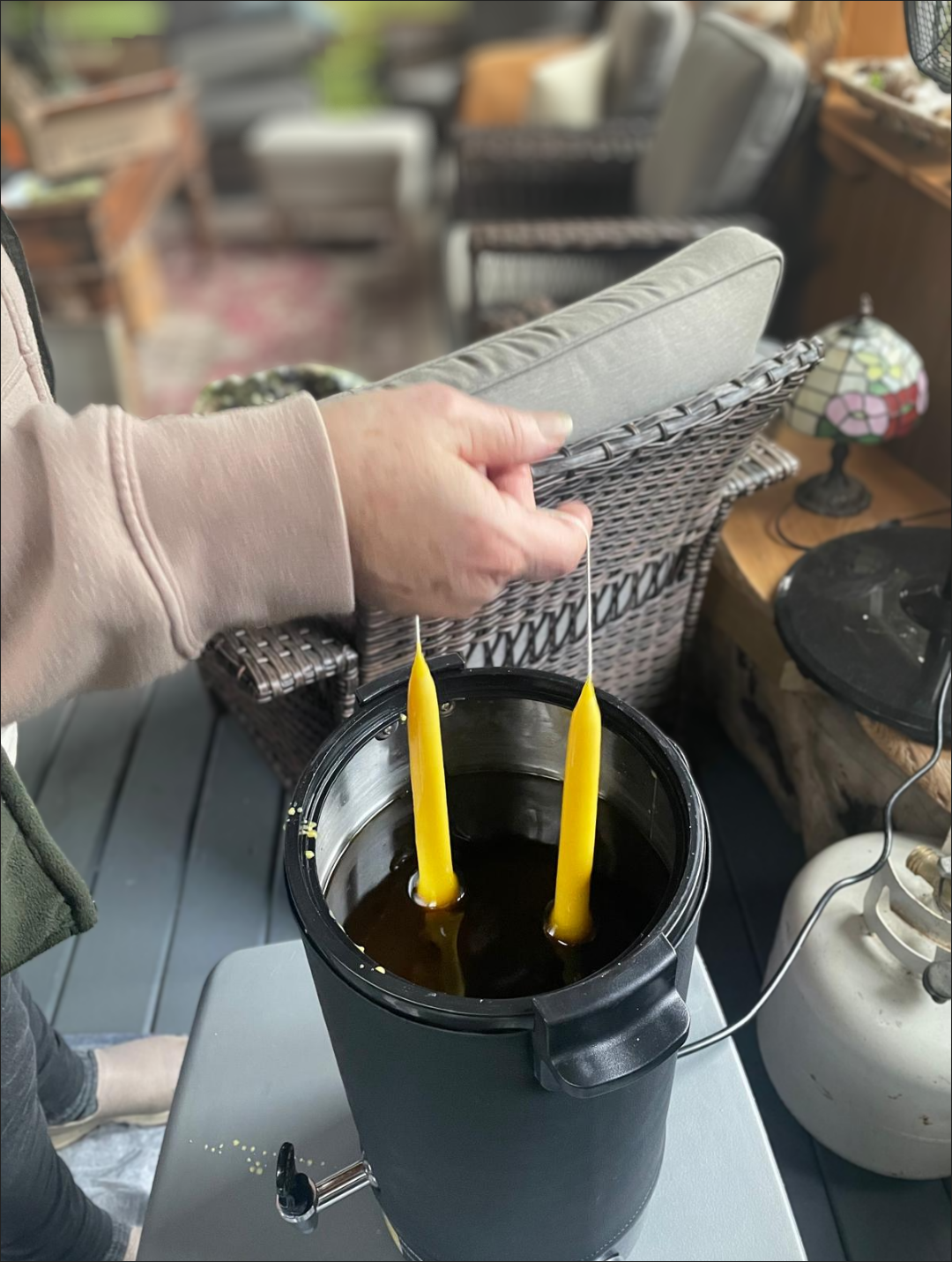 Hands dipping a pair of cotton wicks into warm golden beeswax to form tapers